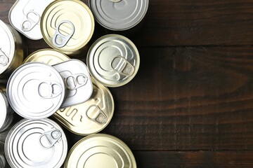 Many closed tin cans on wooden table, flat lay. Space for text