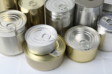 Many closed tin cans on white tiled table, closeup