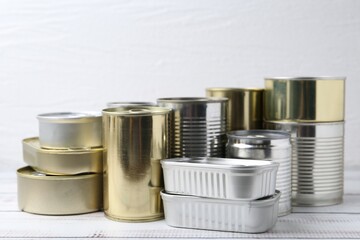 Many closed tin cans on white wooden table, closeup