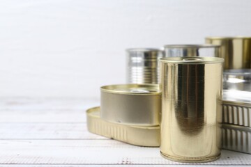 Many closed tin cans on white wooden table, closeup. Space for text