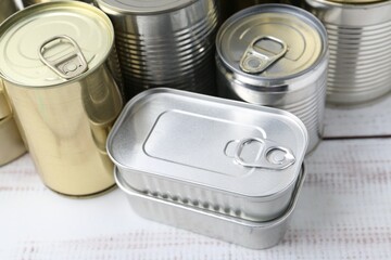 Many closed tin cans on white wooden table, closeup