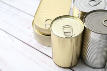 Many closed tin cans on white wooden table, closeup. Space for text