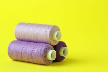 Spools of colorful sewing threads on yellow background, closeup. Space for text