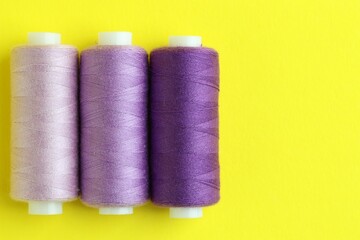 Spools of colorful sewing threads on yellow background, flat lay. Space for text