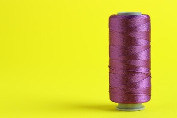 Spool of purple sewing thread on yellow background, space for text