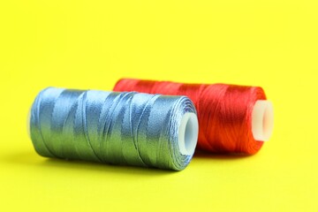 Spools of colorful sewing threads on yellow background, closeup