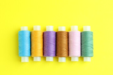 Spools of colorful sewing threads on yellow background, flat lay