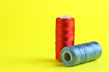 Spools of colorful sewing threads on yellow background, closeup. Space for text