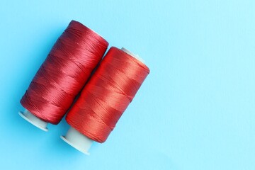 Spools of red sewing threads on light blue background, top view. Space for text