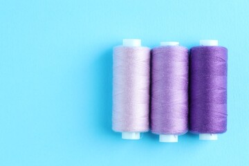 Spools of colorful sewing threads on light blue background, flat lay. Space for text