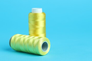 Spools of yellow sewing threads on light blue background, closeup. Space for text