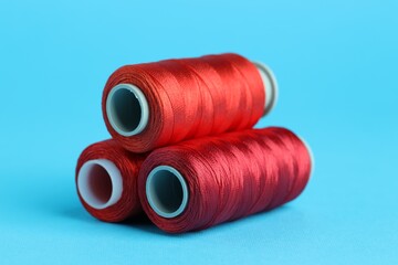 Spools of red sewing threads on light blue background, closeup