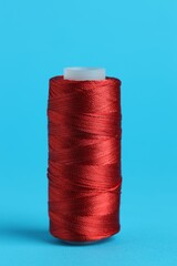 Spool of red sewing thread on light blue background