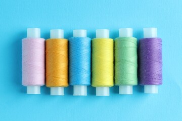 Spools of colorful sewing threads on light blue background, flat lay