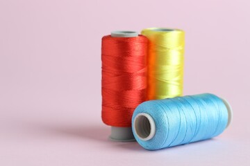 Spools of colorful sewing threads on pink background, closeup. Space for text
