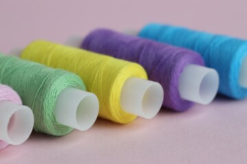 Spools of colorful sewing threads on pink background, closeup