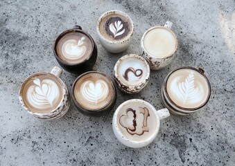 Artful Display of Assorted Coffee Cups Featuring Intricate Latte Art Designs in Variety of Shades and Textures on Rustic Gray Background