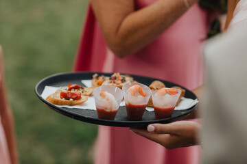 Elegant Event Appetizers with Shrimp Cocktail and Bruschetta on a Black Tray Held by a Server in a Sophisticated Outdoor Setting