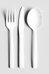 White plastic fork, knife, and spoon on a gray background.