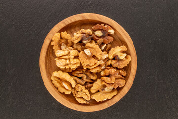 Shelled walnuts with a wooden saucer on a slate stone, close-up, top view.