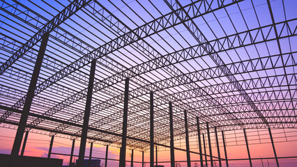 Silhouette metal roof beam with columns of factory building framework structure in construction site against colorful twilight sky background, low angle view