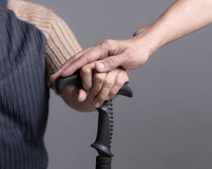 Young man holding hand of old woman with walking stick