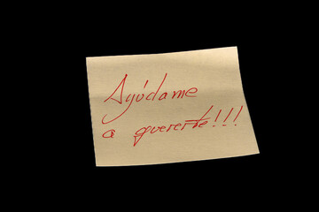 Yellow adhesive paper, similar to a Post-it note, on a black background with the words in Spanish “Ayúdame a quererte” and three exclamation marks  handwritten in red ink.