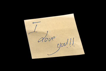 Yellow adhesive paper, similar to a Post-it note, on a black background with the words “I Love You” handwritten in blue ink.