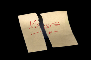 Yellow adhesive paper, similar to a Post-it note, torn into two pieces and reassembled like a puzzle, on a black background with the word "Kisses" handwritten in red ink.
