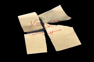 Yellow adhesive paper, similar to a Post-it note, torn into four pieces and reassembled like a puzzle, on a black background with the word "Kisses" handwritten in red ink.