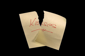 Yellow sticky note, torn into two pieces as if neglected, on a black background with the handwritten words 'Besos' ('Kisses'), written in red ink and underlined. Representing broken, wasted, or reject