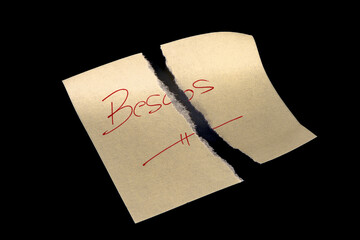 Yellow sticky note, torn into two pieces as if neglected, on a black background with the handwritten words 'Besos' ('Kisses'), written in red ink and underlined. Representing broken, wasted, or reject