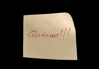 Yellow adhesive paper, similar to a Post-it note, on a black background with the words “Love me” “Quiéreme” in Spanish handwritten in blue ink.