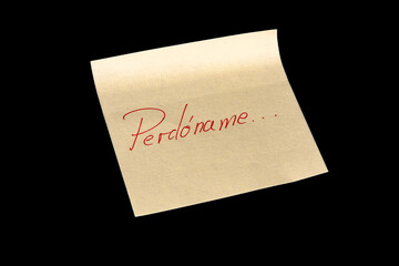 Yellow adhesive paper, similar to a Post-it note, on a black background with the words “Remember me” Recuérdame” in Spanish handwritten in blue ink.