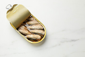 Tasty sprats in tin can on white marble table, top view. Space for text