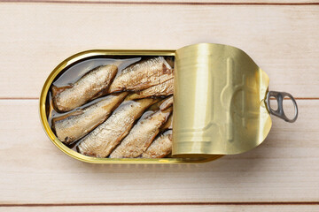 Tasty sprats in tin can on wooden table, top view