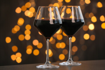 Tasty red wine in glasses on table against dark background with blurred lights, bokeh effect
