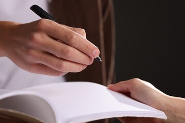 Man signing autograph in notebook on black background, closeup