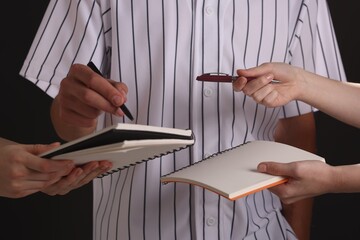 Baseball player signing autograph in notebook against black background, closeup
