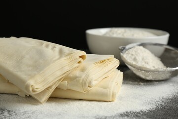 Raw puff pastry dough and flour on dark table against black background, closeup