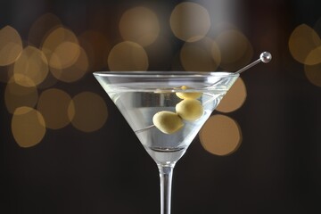 Martini cocktail with olives in glass on blurred background, closeup. Bokeh effect