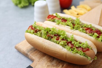 Tasty hot dogs with lettuce, ketchup and potato fries on light grey table, closeup