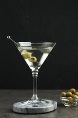 Martini cocktail with olives in glass on grey table against black background