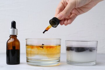 Iodine starch test. Woman dripping iodine into glass of water at white table, closeup