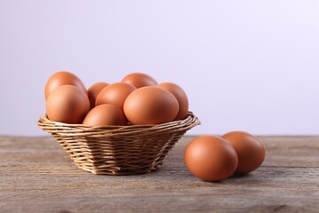 Wicker basket with fresh eggs on wooden table against white background, closeup