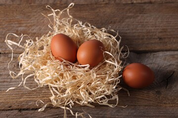 Fresh eggs in nest on wooden table, above view