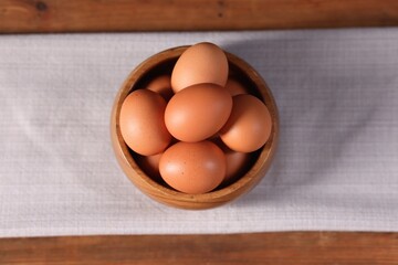 Fresh eggs in bowl on wooden table, top view