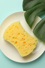 One sponge, plate and monstera leaf on light blue background, top view