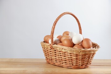 Many raw eggs in basket on wooden table. Space for text