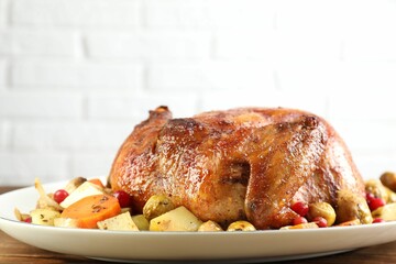 Delicious baked turkey, vegetables and cranberries on wooden table against white brick wall, closeup
